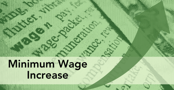 Image of dictonary with focus on the word "wage." Text over top says Minimum Wage Increase, with an Arrow curving upward on right side. 